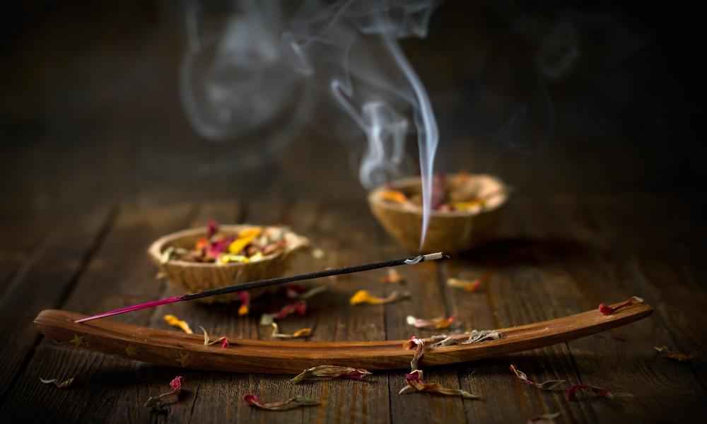Incense stick on a wooden holder beside bowls of puja samagri