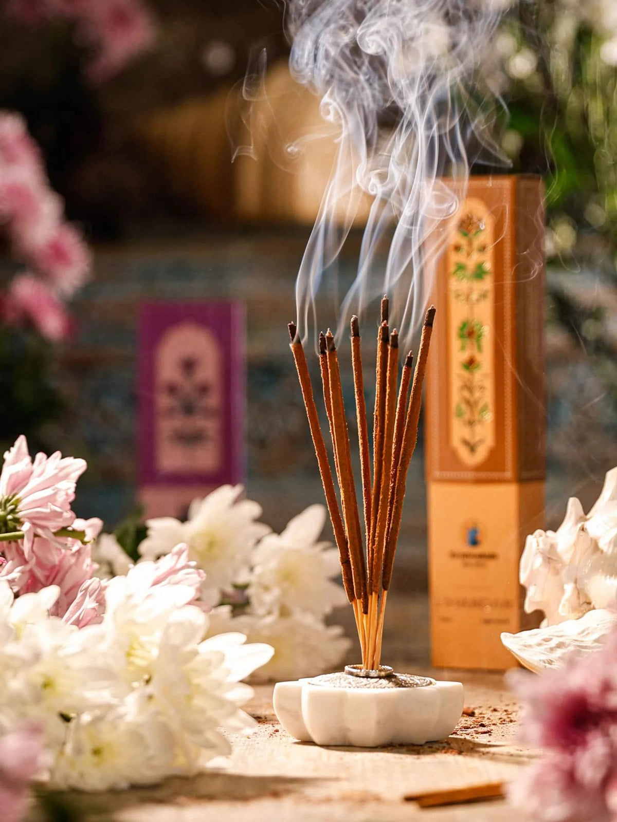 Ishvarya premium agarbatti incense sticks lit beside fresh flowers and the box